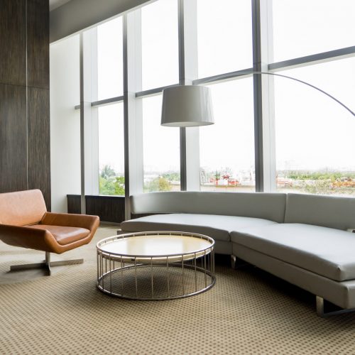 Modern lounge room interior in office building. Room with panoramic window, modern leather chair, white sofa and floor lamp. Downtown workspace design concept